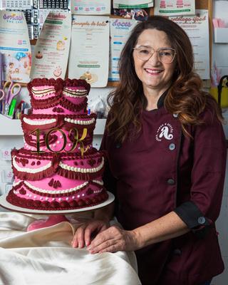 Auris, confeiteira da Auris Doceria, ao lado de um bolo de andar vintage rosa