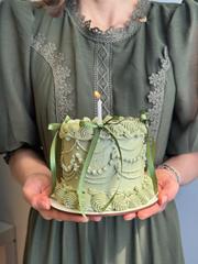 Mulher segurando bentô cake verde vintage com velinha em sessão de fotos