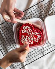 Mãos abrindo marmitinha com bentô de coração vermelho